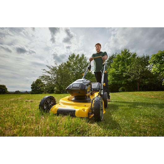 Photo of STANLEY SFMCMS2653B yellow cordless lawn mower in use on grass, front angle outdoors.