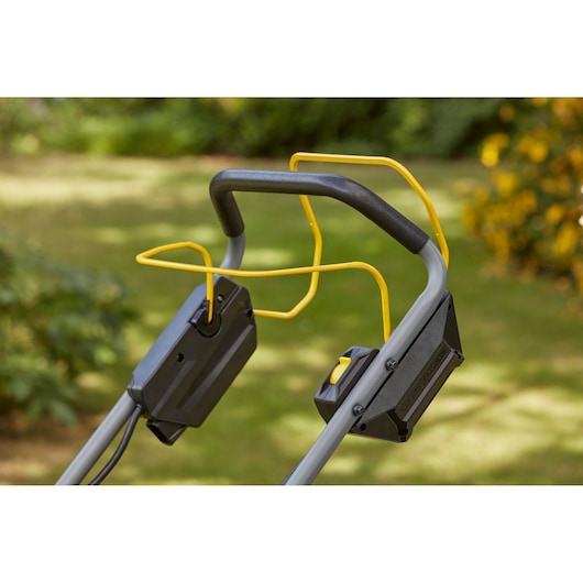 STANLEY SFMCMS2653B mower handle with yellow safety bar and dual control panels, outdoor angle.