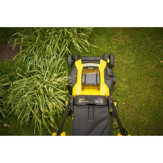 Photo of STANLEY SFMCMW2651M lawn mower on grass, top view showing yellow and black design and battery cover.
