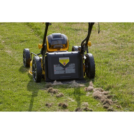 Photo of STANLEY SFMCMW2653B lawn mower rear view on green grass with mulch and warning label visible.