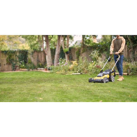 Photo of STANLEY SFMCMWS251M lawn mower in use on grass, yellow and black design, garden background.