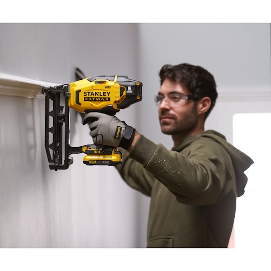 STANLEY SFMCN616D2K cordless nailer, yellow and black, used for wall trim installation, side view.