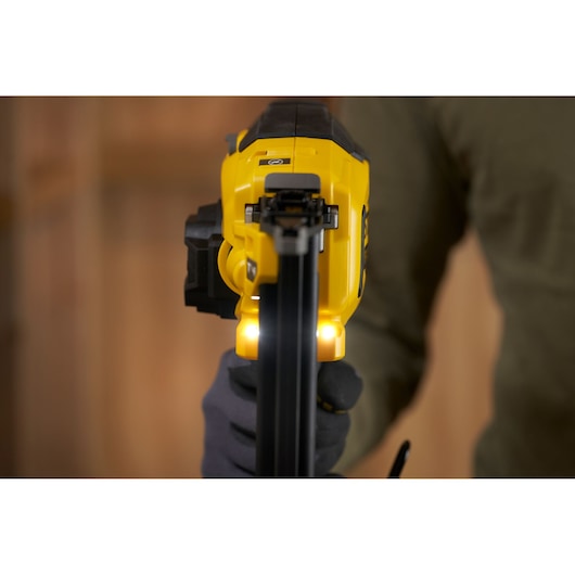 STANLEY SFMCN618B-XJ nail gun front angle, yellow body, LED lights illuminated, gloved hand holding tool.