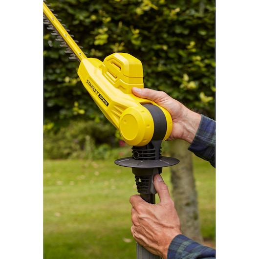 Photo of STANLEY SFMCPH845B hedge trimmer held in hands, showing yellow body and blade outdoors.