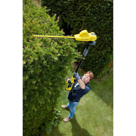 Photo of a person using STANLEY SFMCPH845M1 pole hedge trimmer to trim tall bushes outdoors.