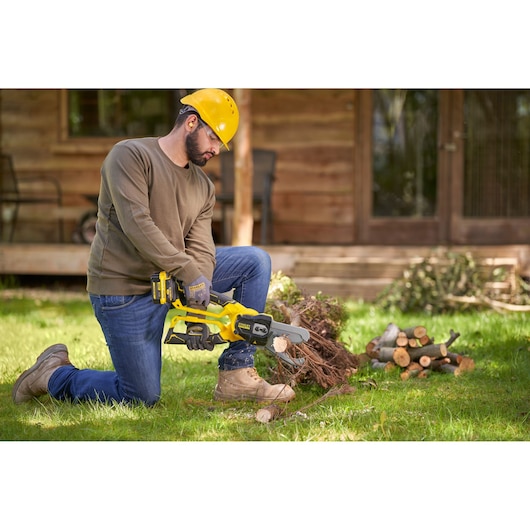 Photo of a person using a STANLEY SFMCPS515B cordless chainsaw to cut branches outdoors on grass.