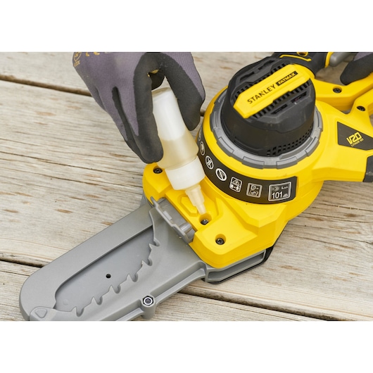 Photo of STANLEY SFMCPS515B chainsaw being oiled at close-up angle, showing yellow body and gray blade.