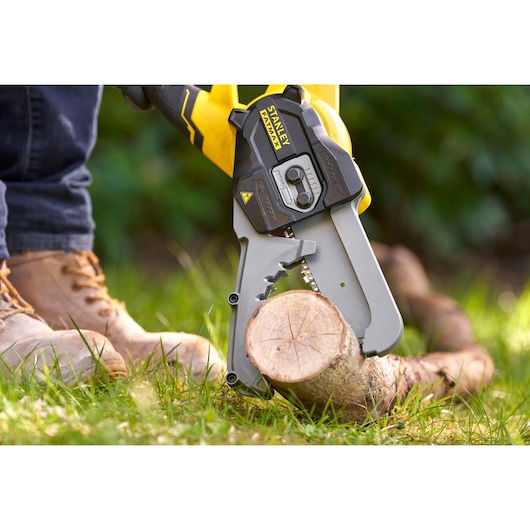 STANLEY SFMCPS515M1 cordless chainsaw cutting a log outdoors, close-up view with person wearing work boots.