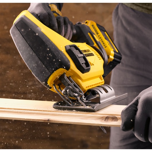 Photo of STANLEY SFMCS600M2K cordless jigsaw in use, cutting wood, close-up of tool and gloved hands.