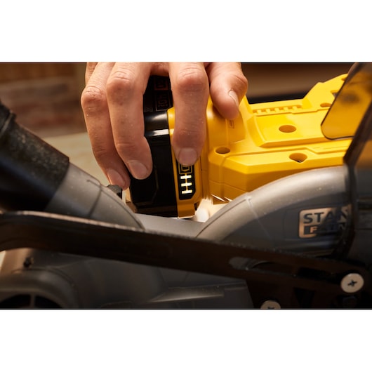 Photo of a hand inserting battery into STANLEY SFMCS701M1 mitre saw, close-up view showing assembly detail.