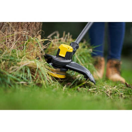 STANLEY SFMCSTB933B grass trimmer close-up, yellow and black, trimming around tree base outdoors.