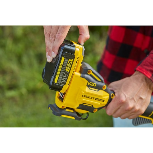 Photo of STANLEY SFMCSTB933B V20 battery being attached to yellow cordless tool outdoors.