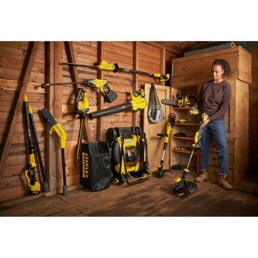 Photo of STANLEY SFMCSTB933M garden tools and accessories neatly arranged in a wooden shed, with person holding trimmer.