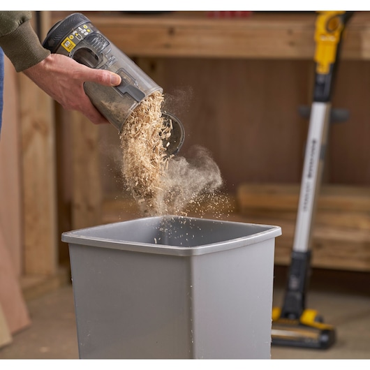 STANLEY SFMCVS001D1 vacuum canister emptied with sawdust into bin, workshop background, side angle.