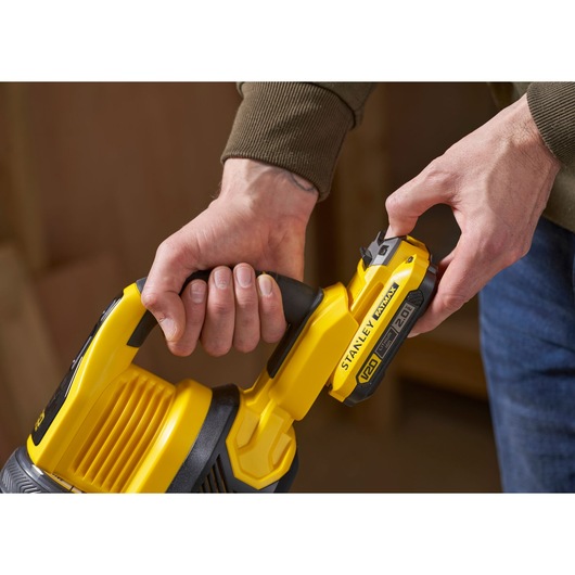 Photo of STANLEY SFMCVS001D1 vacuum with V20 battery being attached, close-up of yellow handle and battery slot.