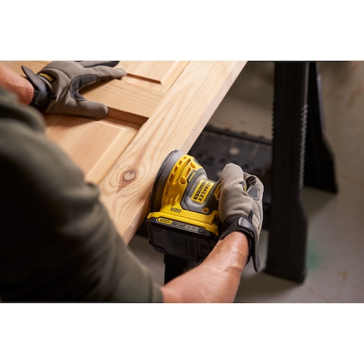 Photo of STANLEY SFMCW220D1S cordless sander in use on wooden board, user wearing work gloves.