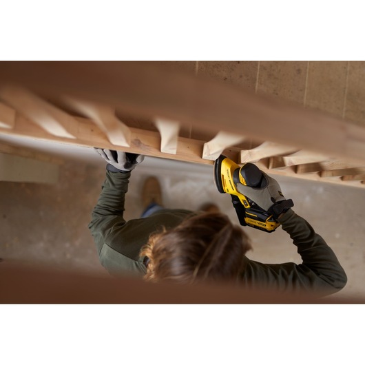 Photo of person using STANLEY SFMCW221D1S cordless sander on wooden railing, wearing gloves.