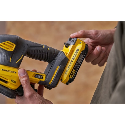 Photo of STANLEY SFMCW221D1S cordless sander V20, yellow and black, held in hands, side close-up.