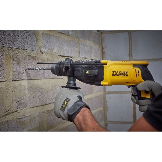 Photo of STANLEY SFMEH210K-QS rotary hammer drill being used on a brick wall, yellow and black design.
