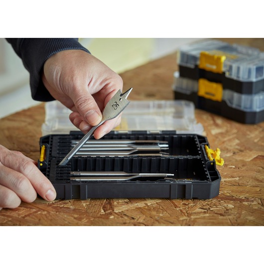 STANLEY STA88556 drill bit set in black case, hand holding flat wood drill bit, case open on wood surface.