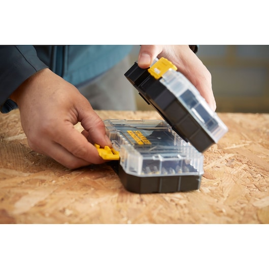 STANLEY STA88558 clear plastic organizer box with yellow latch being opened on a wooden surface