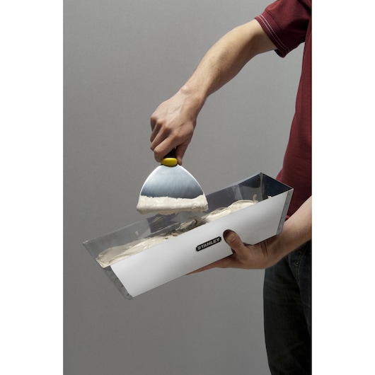 Photo of STANLEY STHT0-05867 taping knife in use, scooping plaster from a metal mud pan.