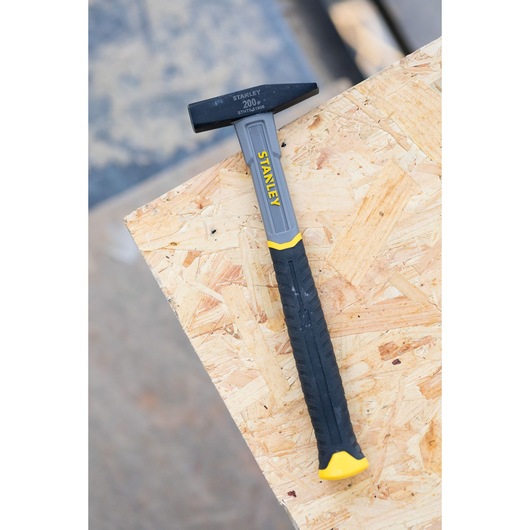 STANLEY STHT0-51906 hammer with black and yellow handle, side view, on plywood board.