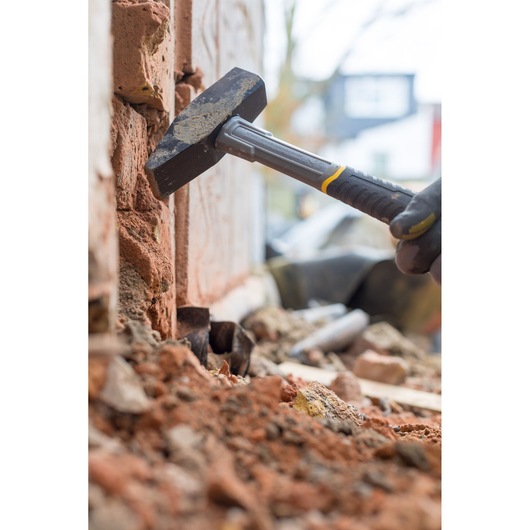 STANLEY STHT0-51910 club hammer with black and yellow handle shown breaking bricks during masonry work.