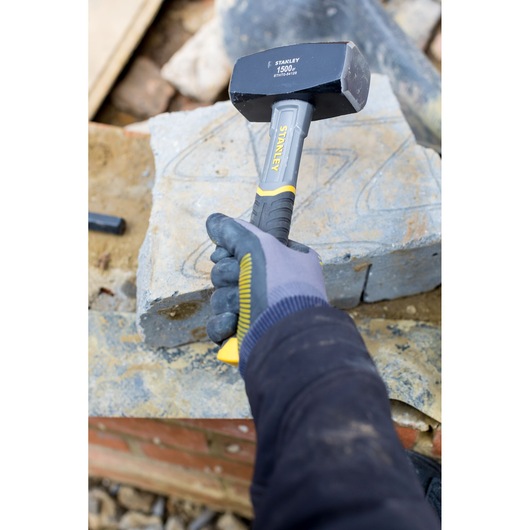 STANLEY STHT0-54128 sledge hammer with yellow and black handle held by gloved hand on stone construction site.
