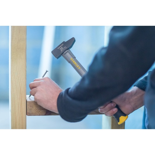 Photo of STANLEY STHT0-54129 hammer driving nail into wooden beam, close-up of worker’s hands.