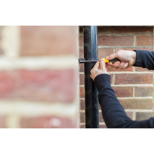 STANLEY STHT0-60273 screwdriver used to tighten a pipe bracket against a brick wall, close-up photography.