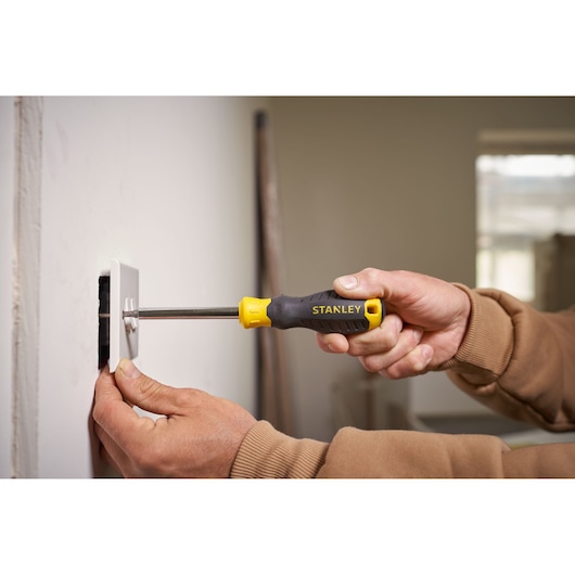 Stanley STHT0-70885 screwdriver with yellow-black handle used to install wall plate, close-up photography.