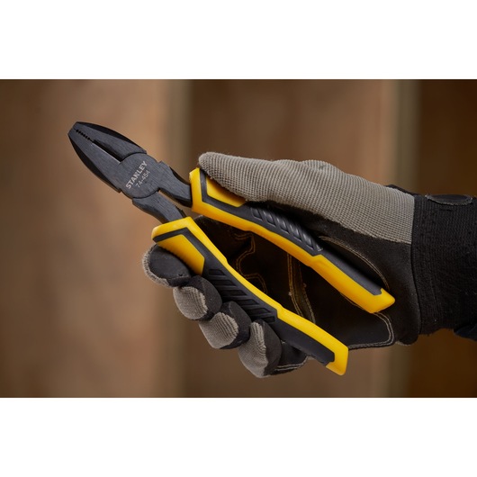 Stanley STHT0-74456 combination pliers held in gloved hand, yellow and black handle, close-up photo.