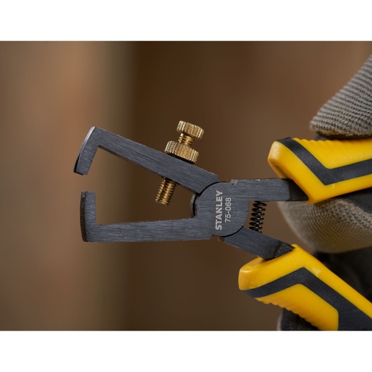 Photo of STANLEY STHT0-75068 wire stripper with yellow and black handles held in a gloved hand.