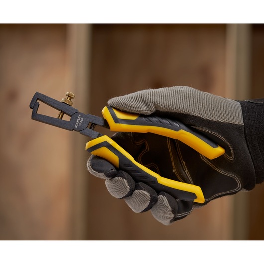 STANLEY STHT0-75068 wire stripper pliers with yellow and black handles, side angle, held by gloved hand.