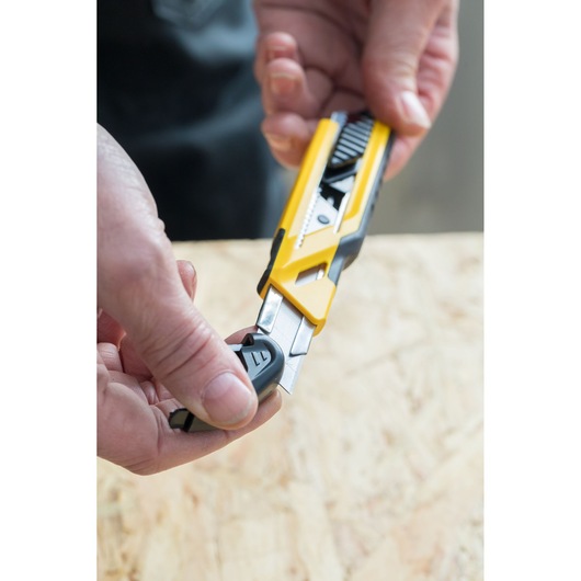 STANLEY STHT10266-0 utility knife with yellow and black body, close-up in hand, blade being adjusted.