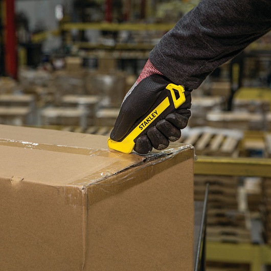 STANLEY STHT10356 yellow utility knife cutting tape on a cardboard box, warehouse background, product in use.