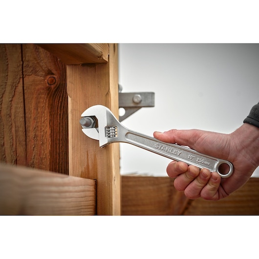 STANLEY STHT13121-0 adjustable wrench tightening bolt on wooden structure, close-up action.