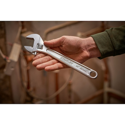 Photo of STANLEY STHT13156-0 adjustable wrench, 250mm, held in hand with background of copper pipes.