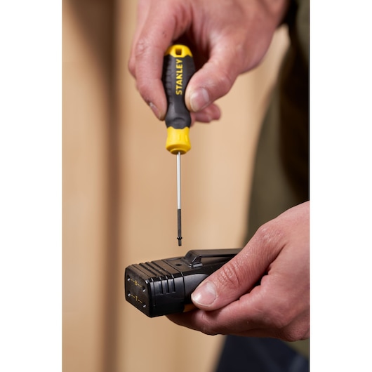 Photo of STANLEY STHT16151-0 screwdriver with yellow and black handle in use on a black electronic device held by hand.