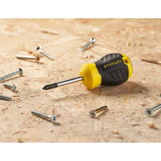 STANLEY STHT16154-0 stubby Phillips screwdriver with black and yellow handle on wood surface with scattered screws.