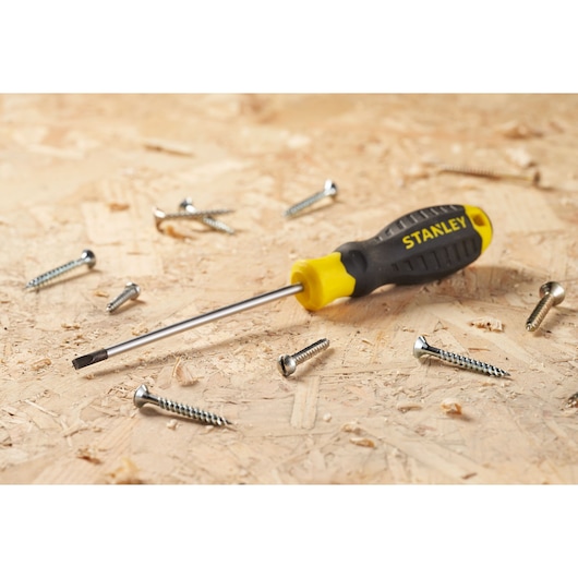 STANLEY STHT16195-0 black and yellow screwdriver on wood surface with metal screws, front angle.