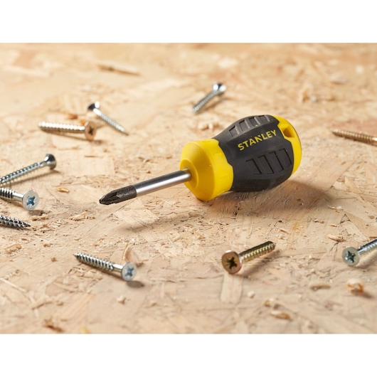 STANLEY STHT16196-0 screwdriver with yellow and black handle resting on wood with scattered screws.