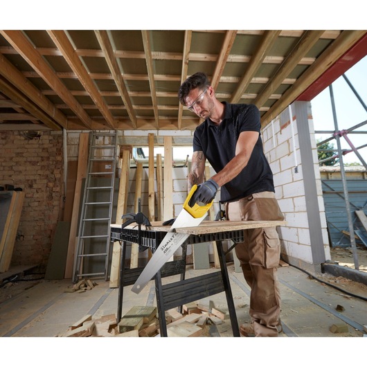STANLEY STHT20354-1 hand saw with yellow handle in use cutting wood on a construction site.