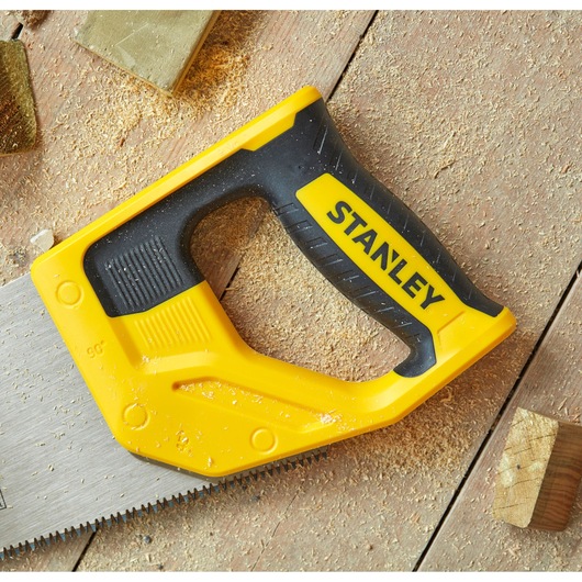 STANLEY STHT20355-1 hand saw with yellow and black handle on wood surface with sawdust.