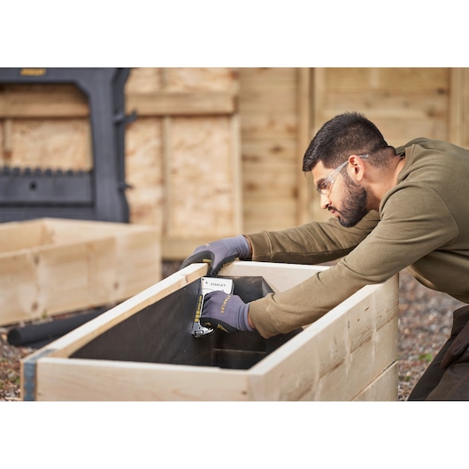 Photo of STANLEY STHT6-70410 hand stapler used for woodworking, person stapling liner inside wooden planter outdoors.
