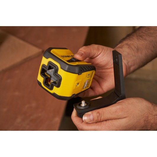 STANLEY STHT77611-0 yellow laser level held in hands with mounting bracket, photography close-up.
