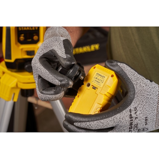Photo of STANLEY STHT77616-0 yellow laser level held by gloved hands, front assembly visible.