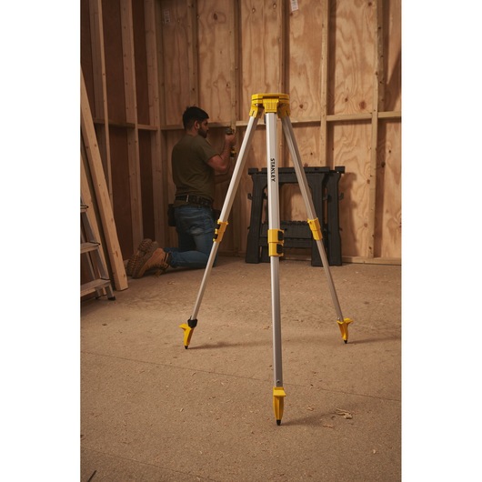 STANLEY STHT77625-1 tripod stand with yellow accents, positioned in a wooden construction room.