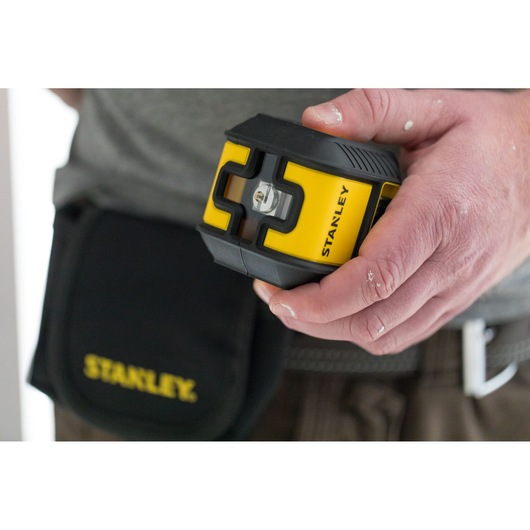 STANLEY STHT77648-1 yellow and black laser level held in hand, tool pouch visible on belt.